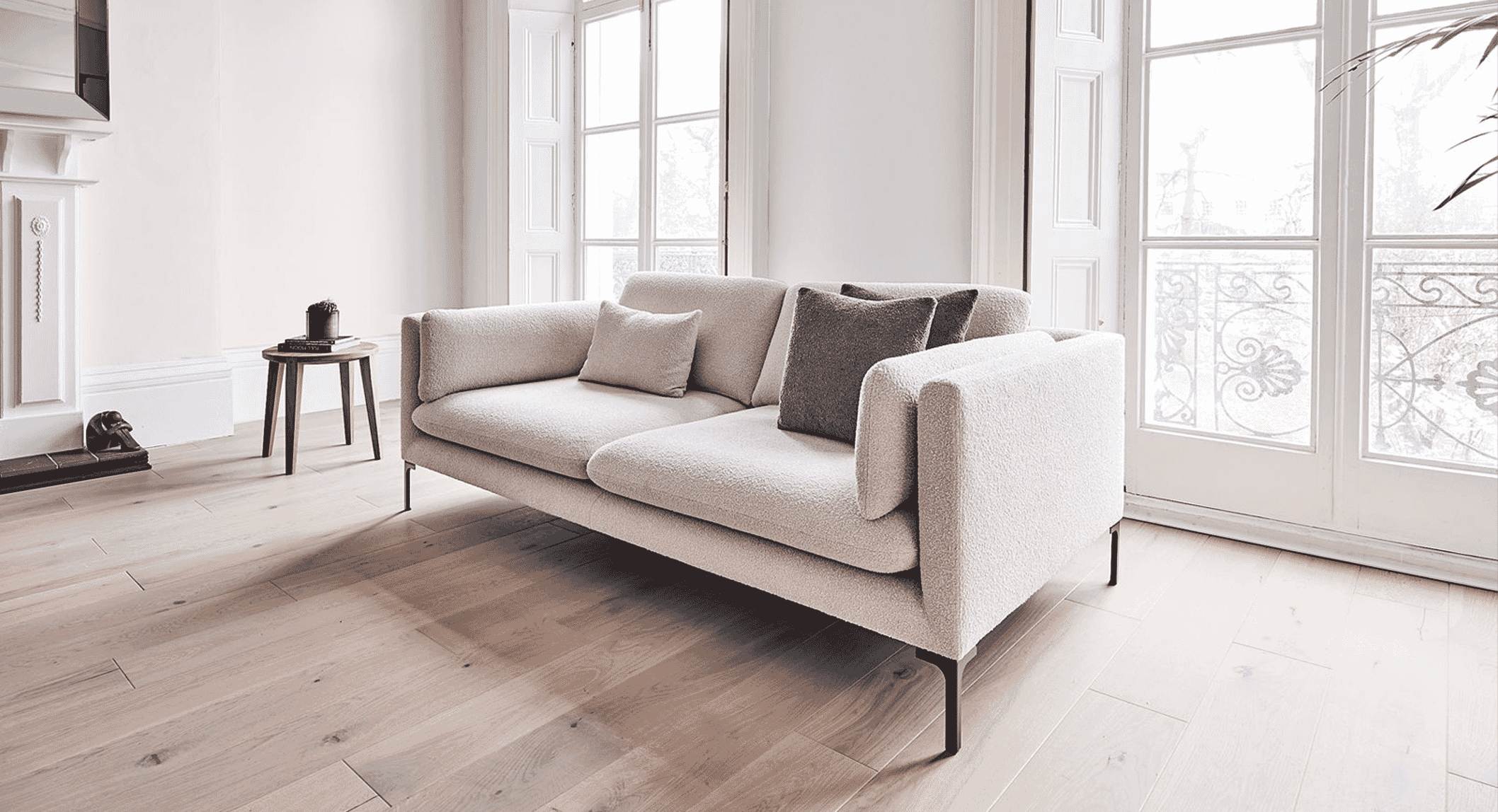 Modern beige bouclé sofa in a sunlit minimalist living room with large windows.