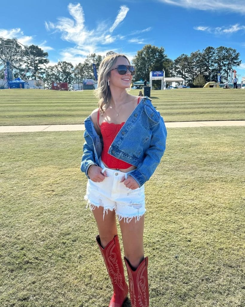 Woman in a red crop top, denim jacket, and red cowboy boots at a festival.