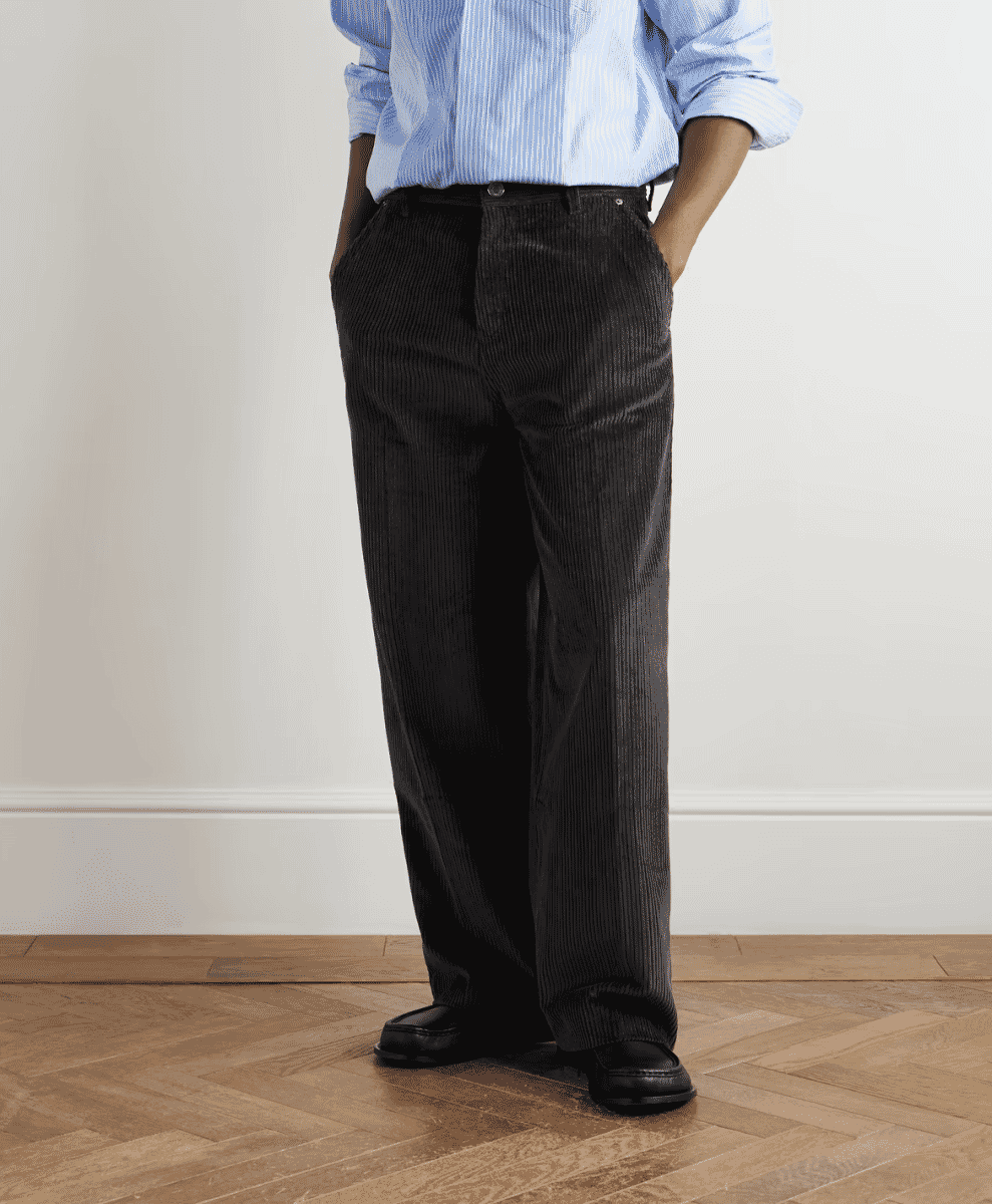 A man wearing dark corduroy trousers paired with a blue striped shirt.