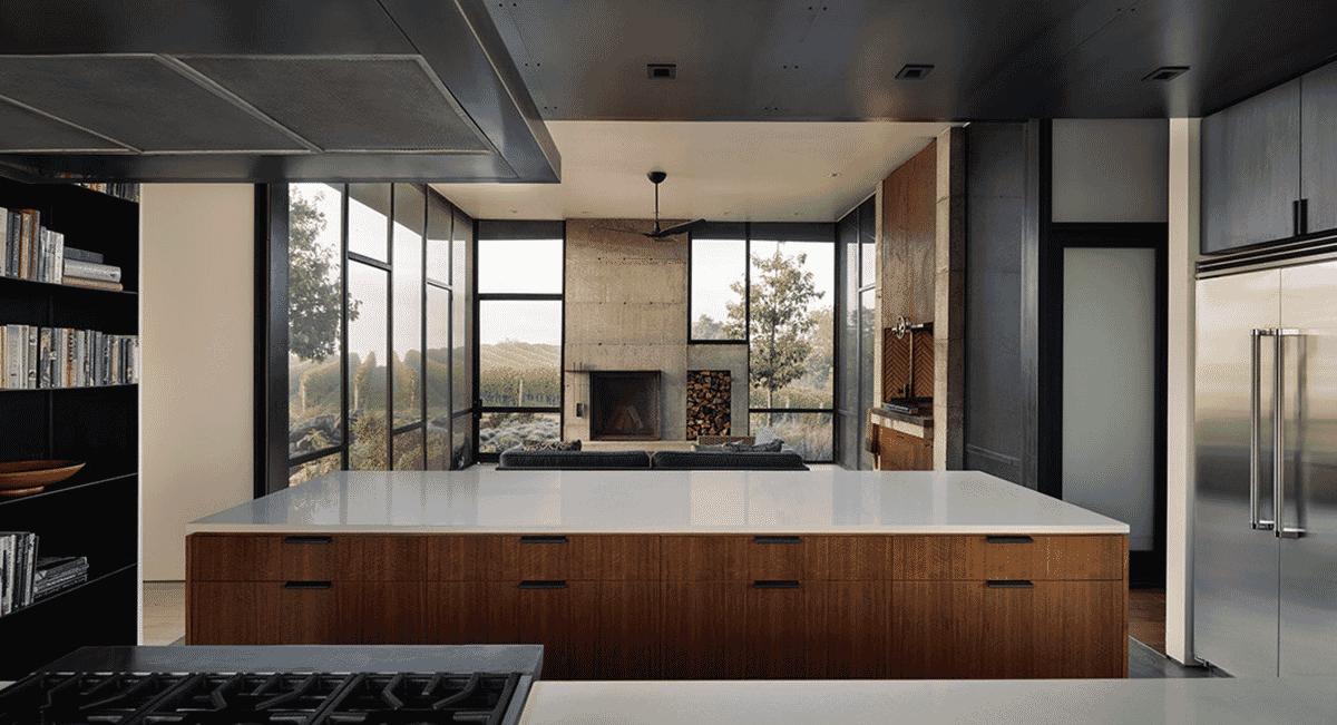 Minimalist open-plan kitchen with warm wood cabinetry and expansive windows overlooking rolling hills.