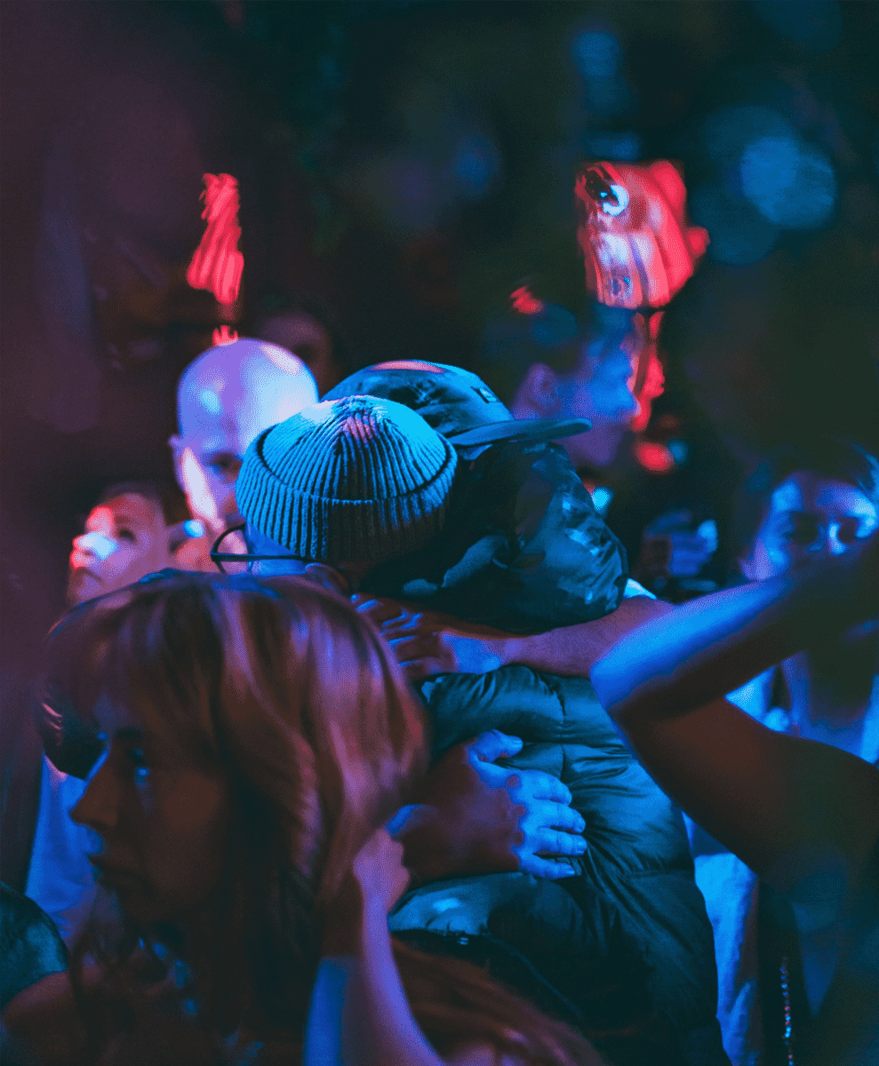 A crowd in a dimly lit club with blue and red lighting wearing streetwear.