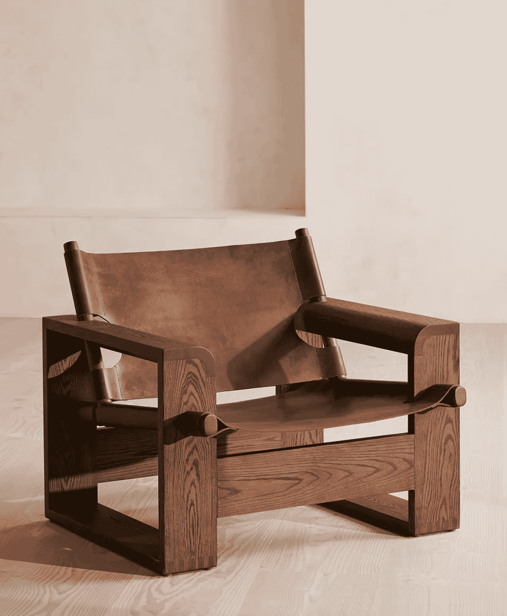 Detail shot of a minimalist wooden armchair featuring brown leather straps against a neutral background.