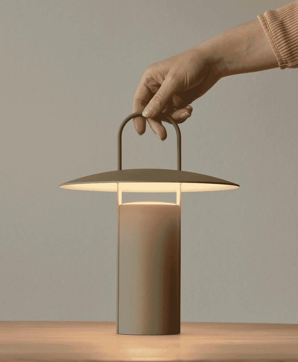 A person holding the handle of a modern portable lamp.
