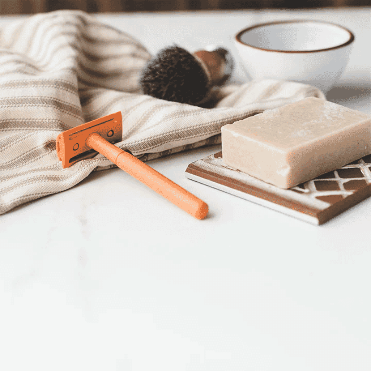 An orange Shoreline safety razor resting on a striped towel in a minimalist bathroom setting.