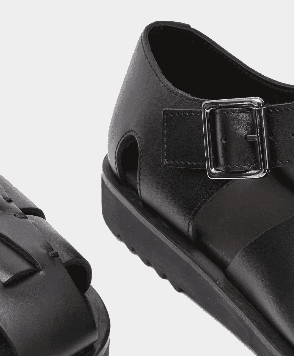 Detail shot of a black leather sandal with a chunky sole and silver buckle.