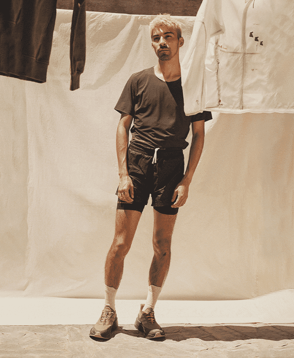 Male model wearing layered black shirts, white socks, and collaboration sneakers against a clothing rack.