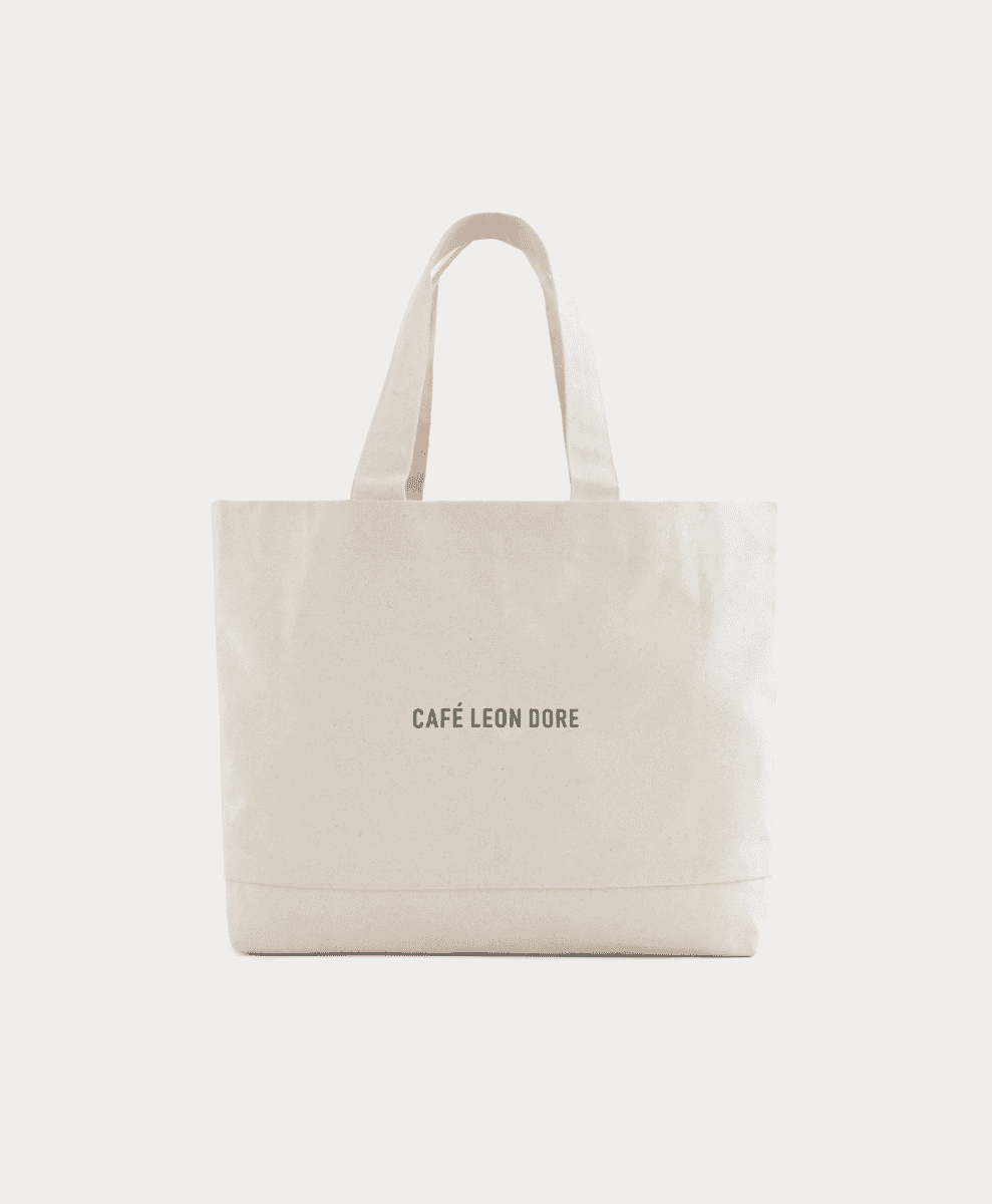 A cream canvas tote bag with gray Café Leon Dore typography.
