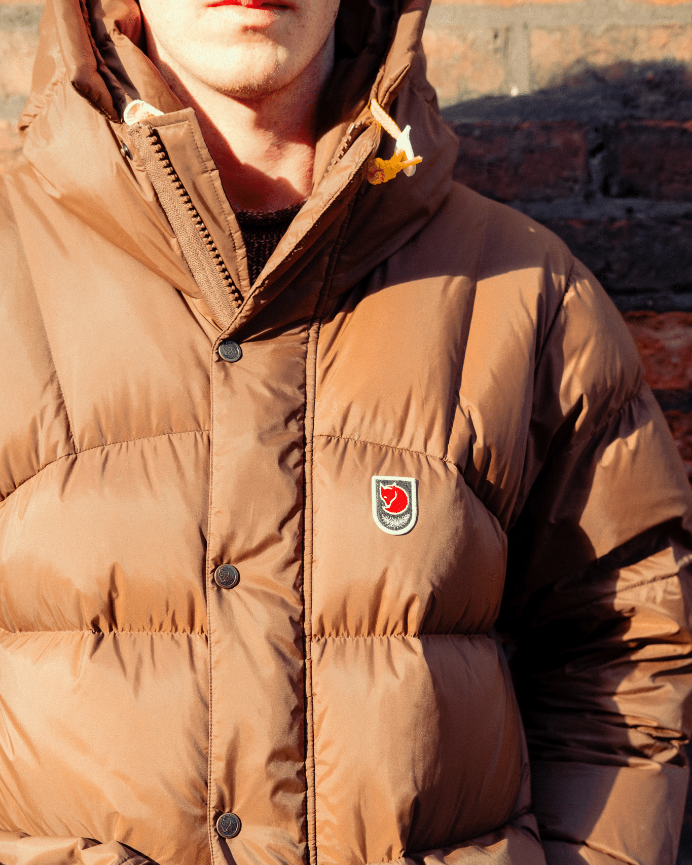 Macro shot of the red Fjällräven fox logo and hood drawstrings on a brown puffer jacket.