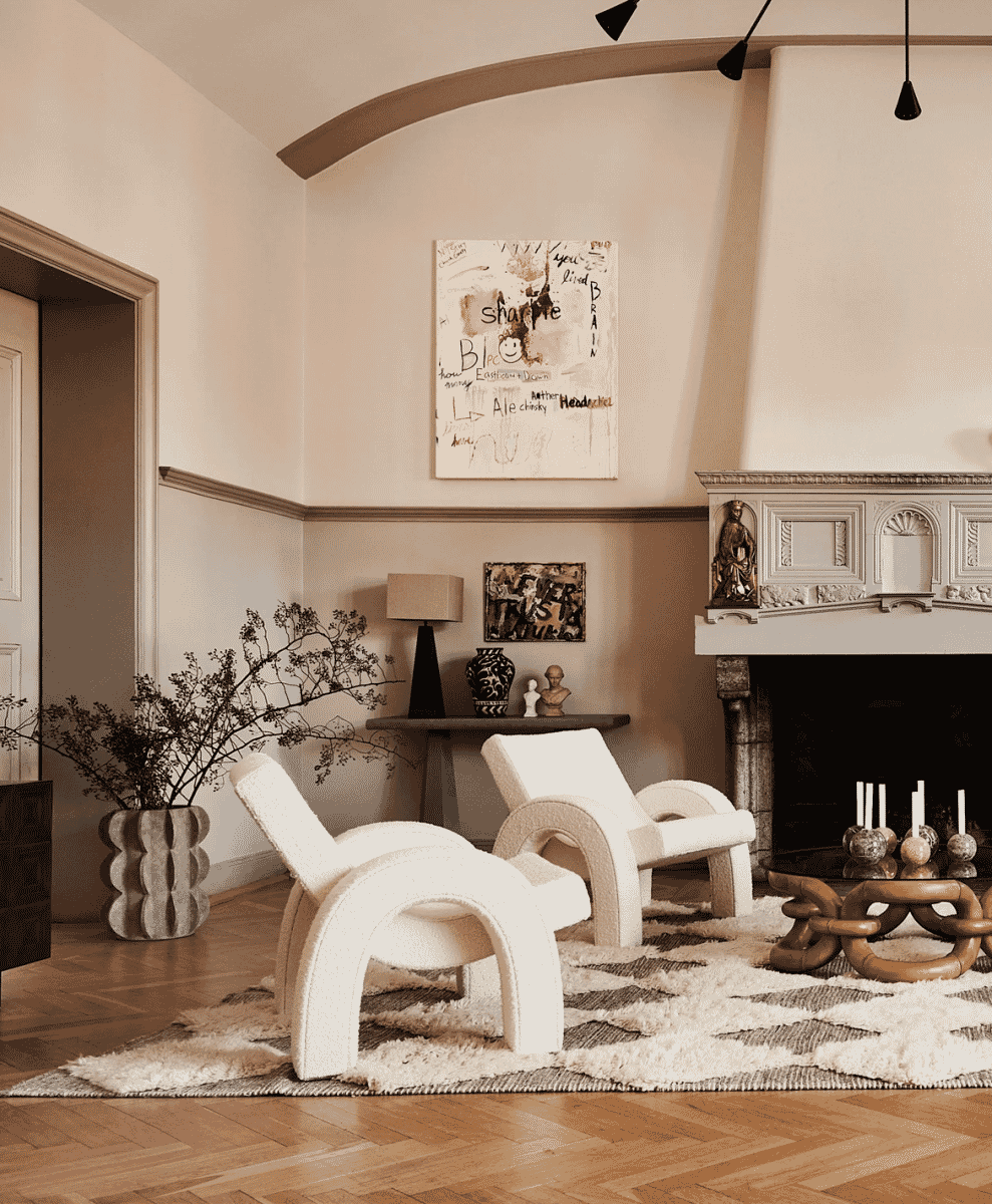 A modern living room with white sculptural chairs, a patterned Rya rug, and an ornate fireplace.