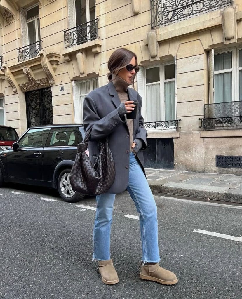 Woman in an oversized grey blazer, light-wash flared jeans, and tan Ugg boots walking on a street in Paris.
