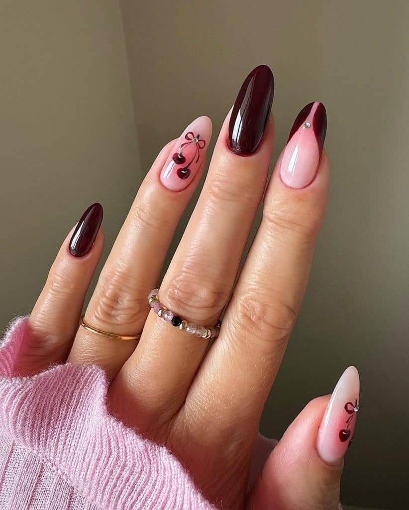 Hand with burgundy and nude cherry-themed nail art paired with a pink ribbed sweater.