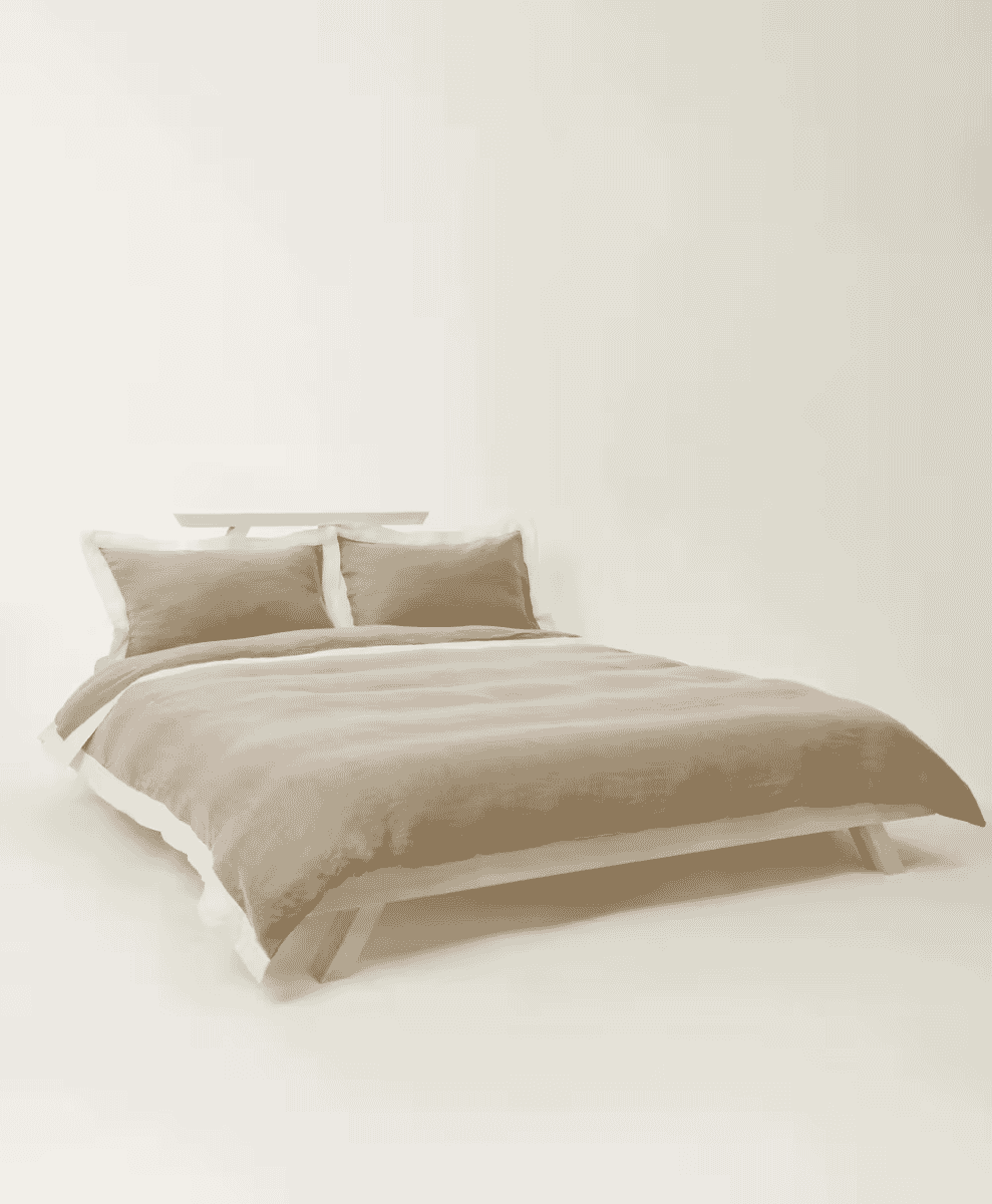 A minimalist bed with beige linen bedding against a plain white background with soft lighting.