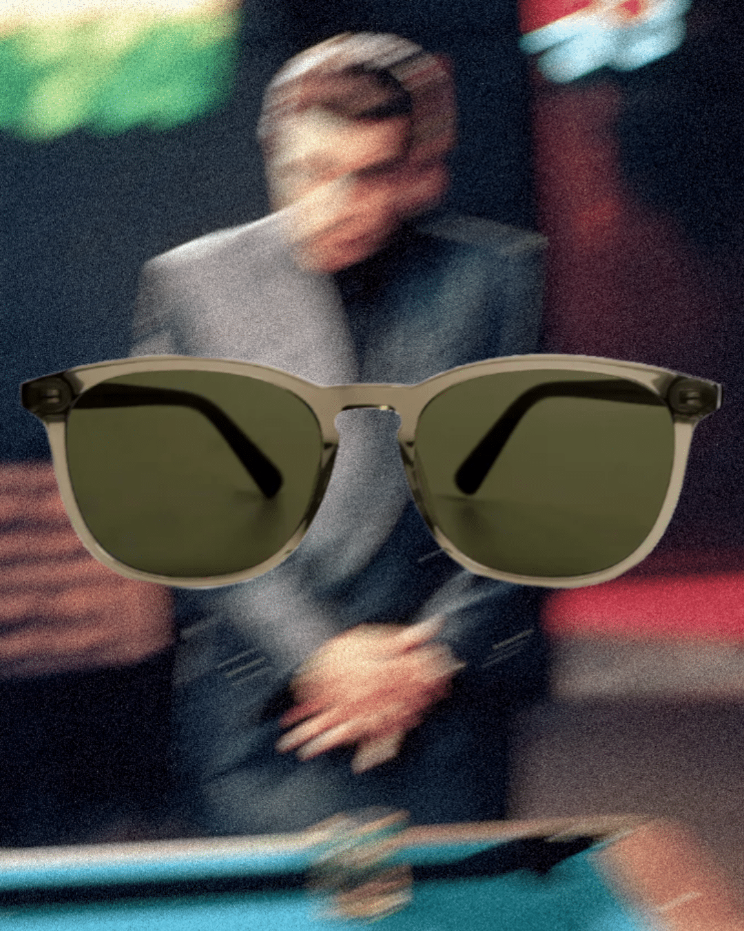 Translucent olive-tinted sunglasses styled with a blurred man in a sharp suit.