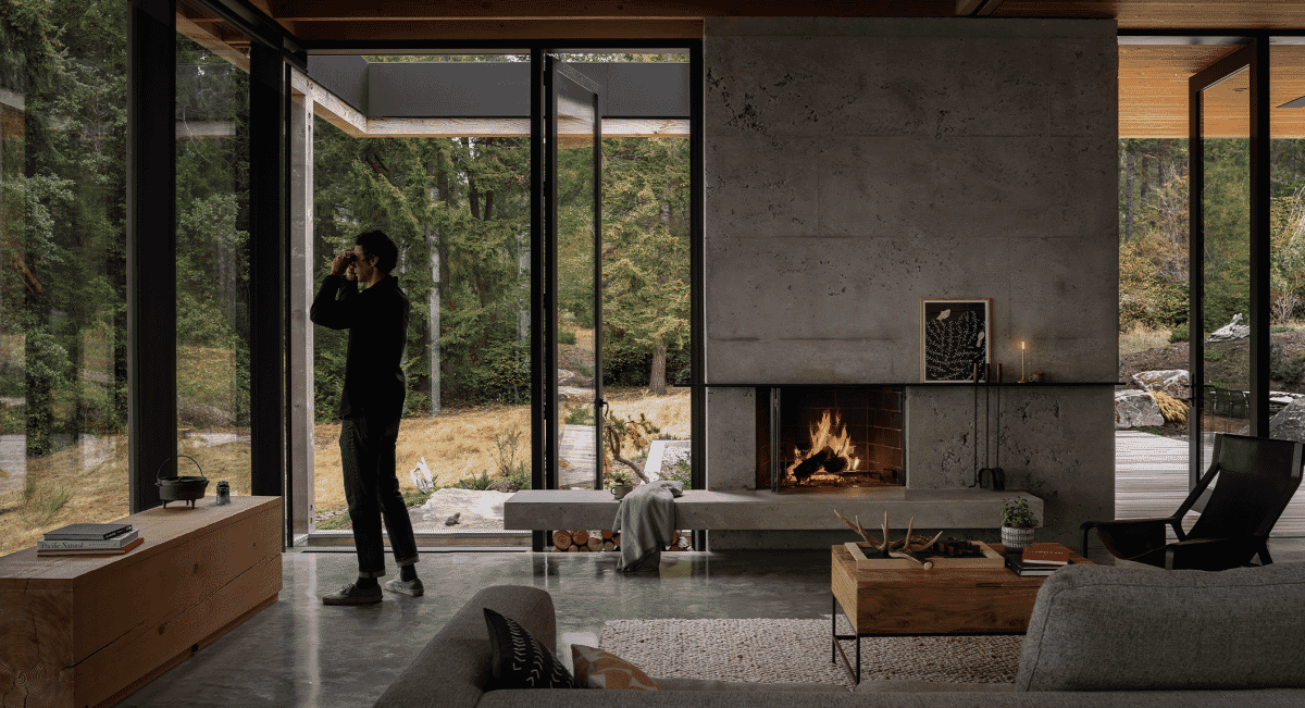 A man in a black long-sleeve top and dark pants standing in a concrete-walled living room.