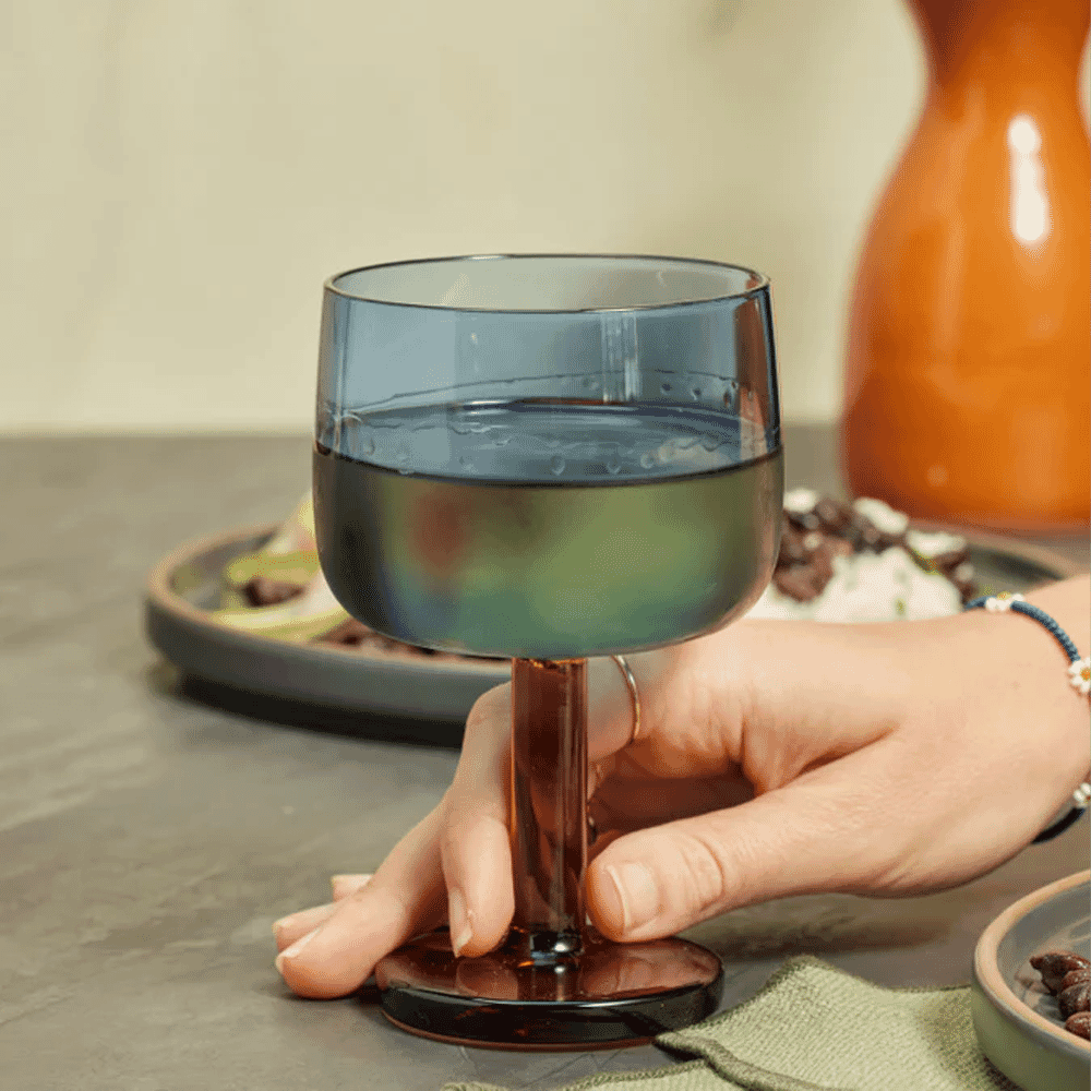 A person holding a blue-tinted glass at a dinner table with soft lighting.