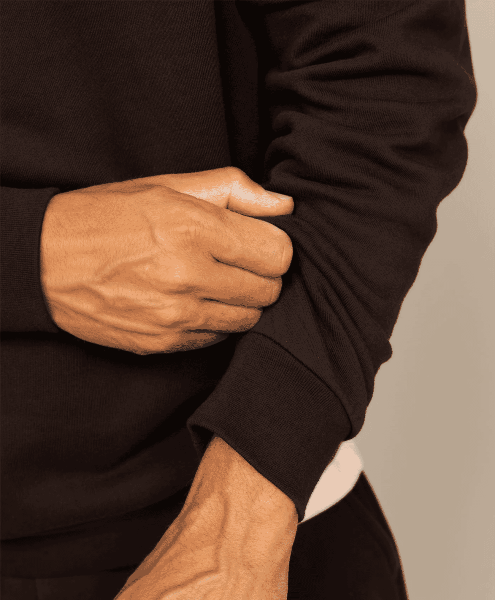 Close-up of a man adjusting the sleeve of a dark brown ribbed-knit top.