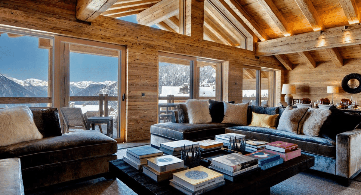 Luxury wood-paneled living room with plush sofas and large windows overlooking snow-capped peaks.
