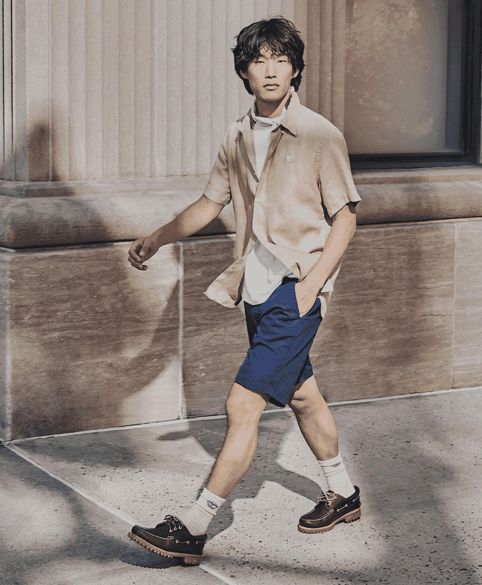 Man walking on a city sidewalk in a beige shirt and brown Timberland boat shoes with thick lug soles.