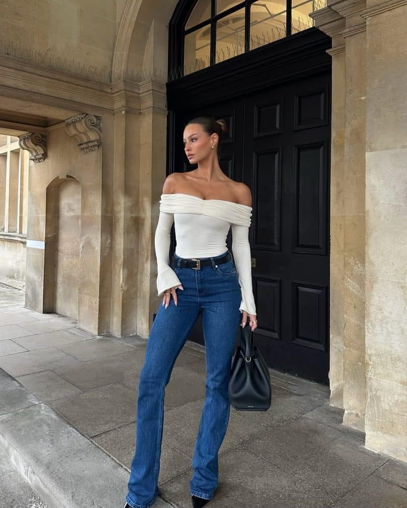 Woman wearing an off-the-shoulder white top with flared sleeves and blue flare jeans.