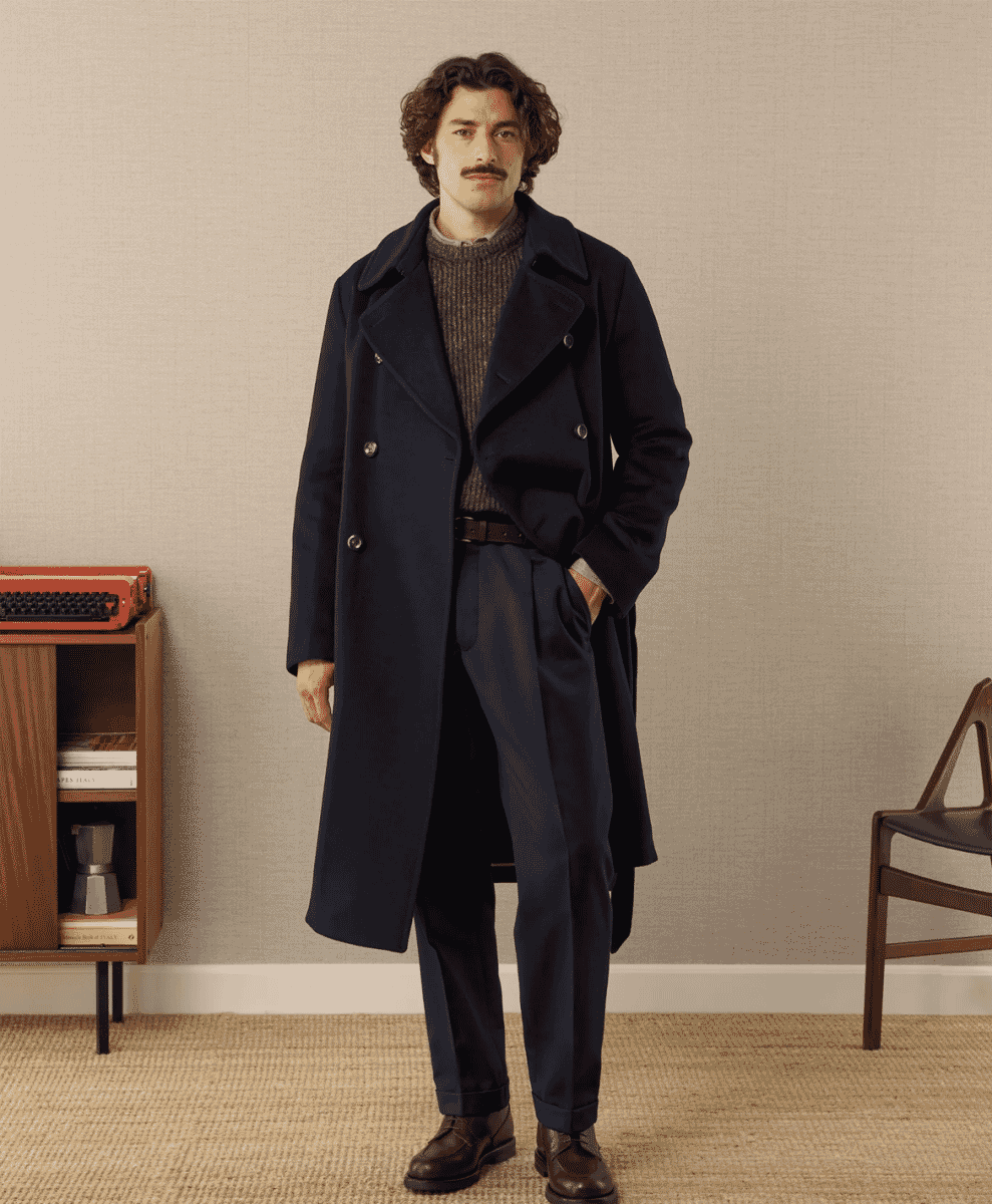 A man wearing a navy double-breasted wool coat over a ribbed sweater.