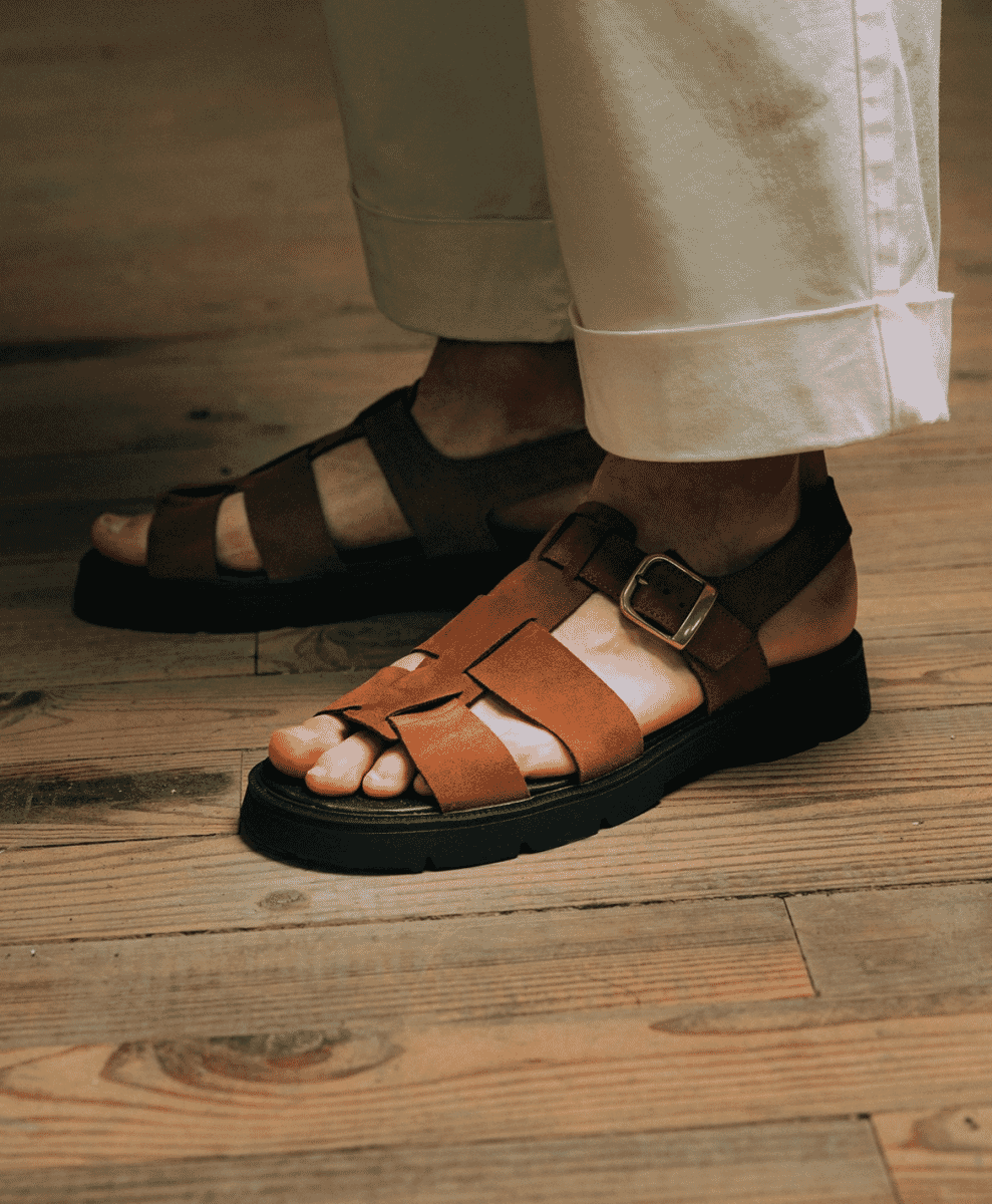 Close-up of brown leather strappy sandals with thick soles paired with rolled-up white trousers.