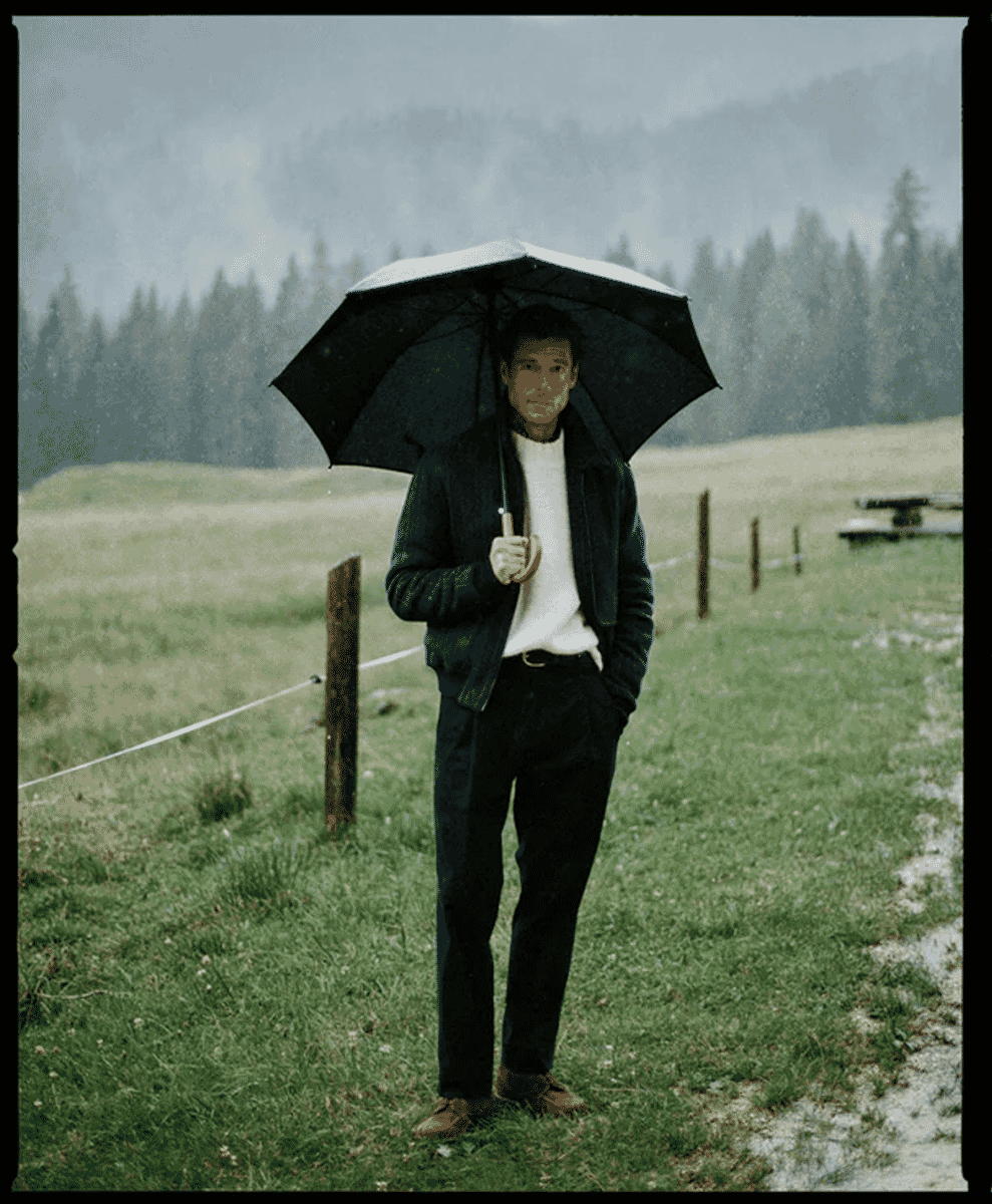 Man with a black umbrella standing in a rainy field.