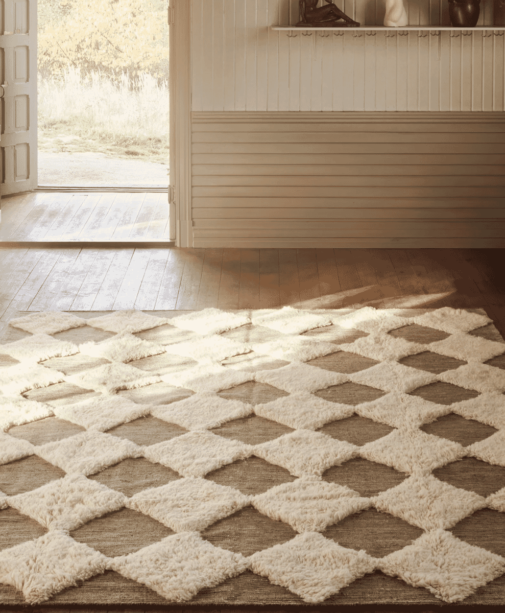 A close-up of a plush diamond-patterned Rya rug in cream and beige tones on a wooden floor.