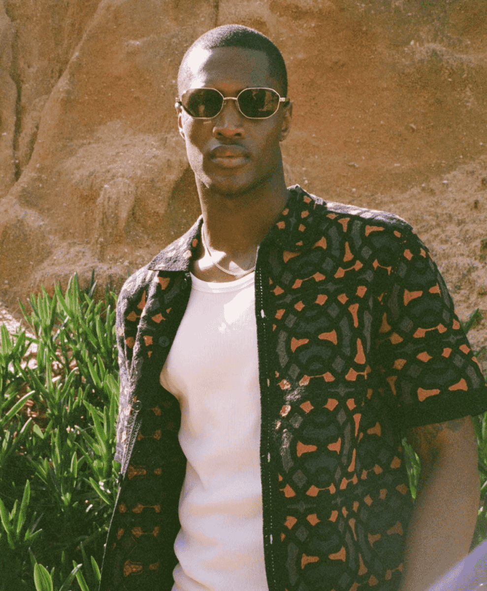 Close-up of a man wearing a black and orange patterned short-sleeve jacket with sunglasses.