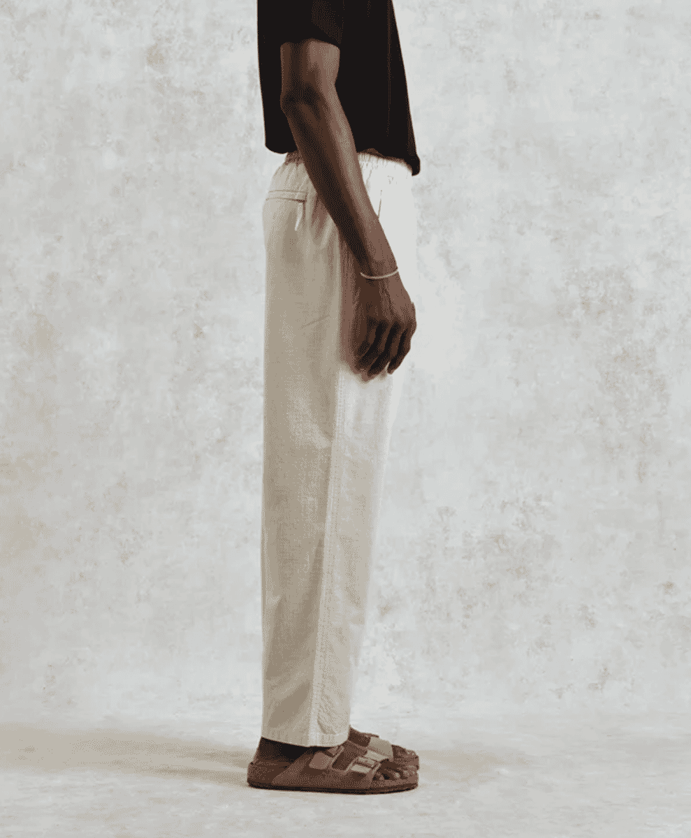 Profile view of a man wearing off-white linen drawstring trousers and a black t-shirt.