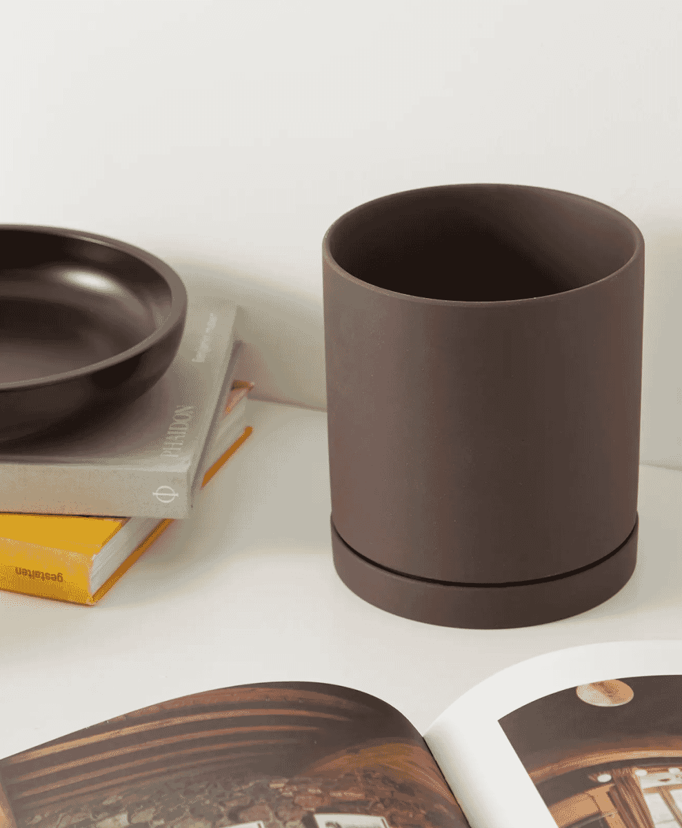 Matte charcoal-colored Sekki Plant Pot next to stacked books.