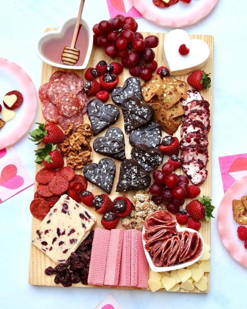 A Valentine's themed charcuterie board featuring heart-shaped cheeses, fruits, and crackers.