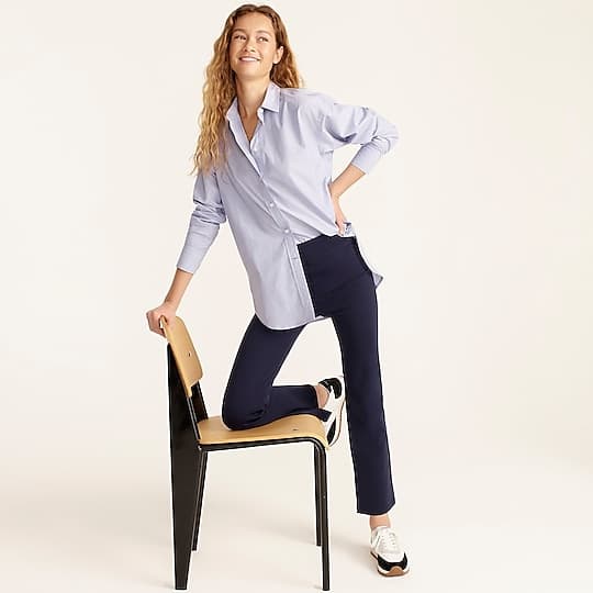 Woman sitting in a light blue oversized shirt and navy blue trousers.