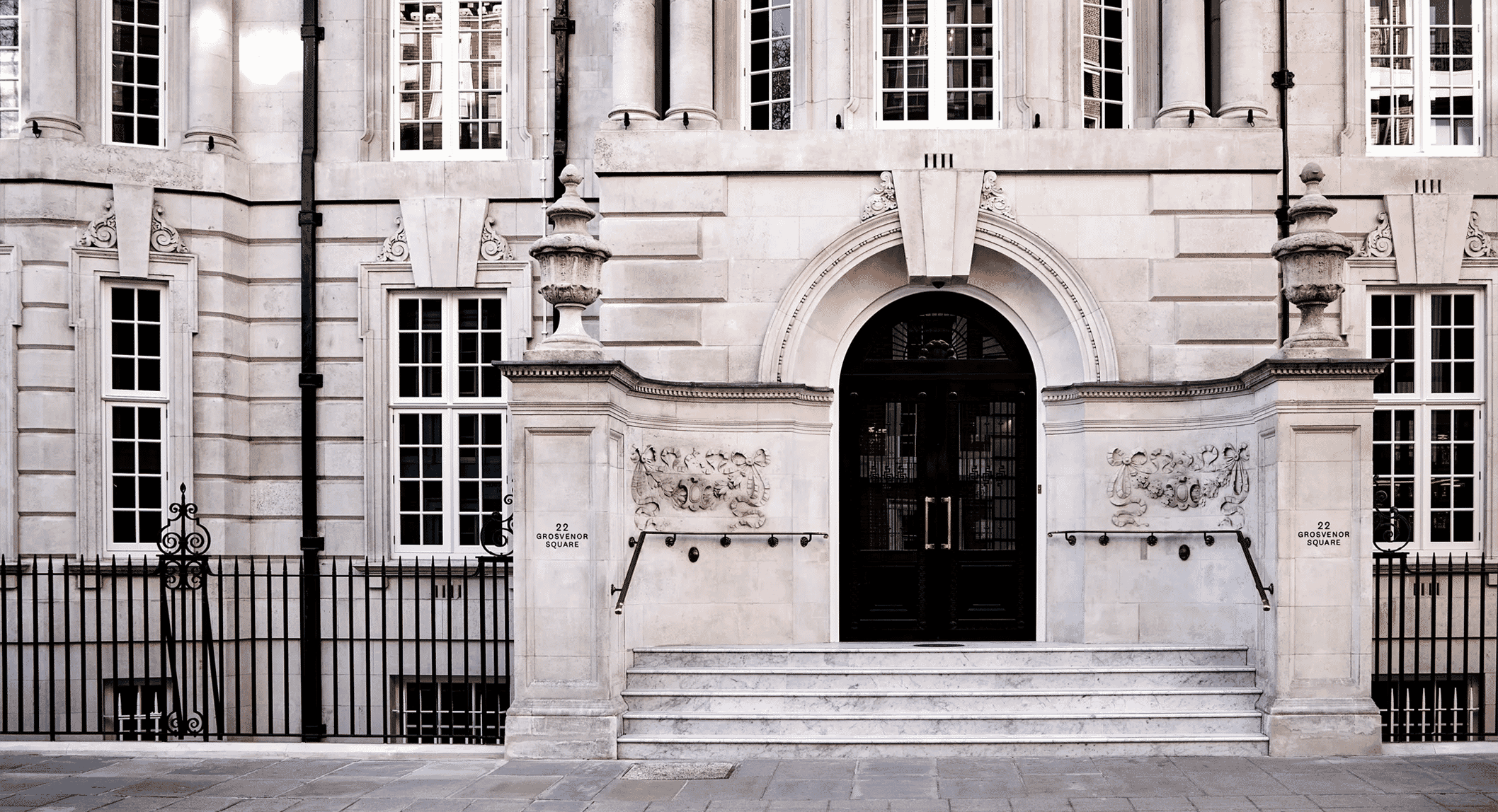 Front view of the classical stone building at 22 Grosvenor Square featuring ornate columns and black iron railings.