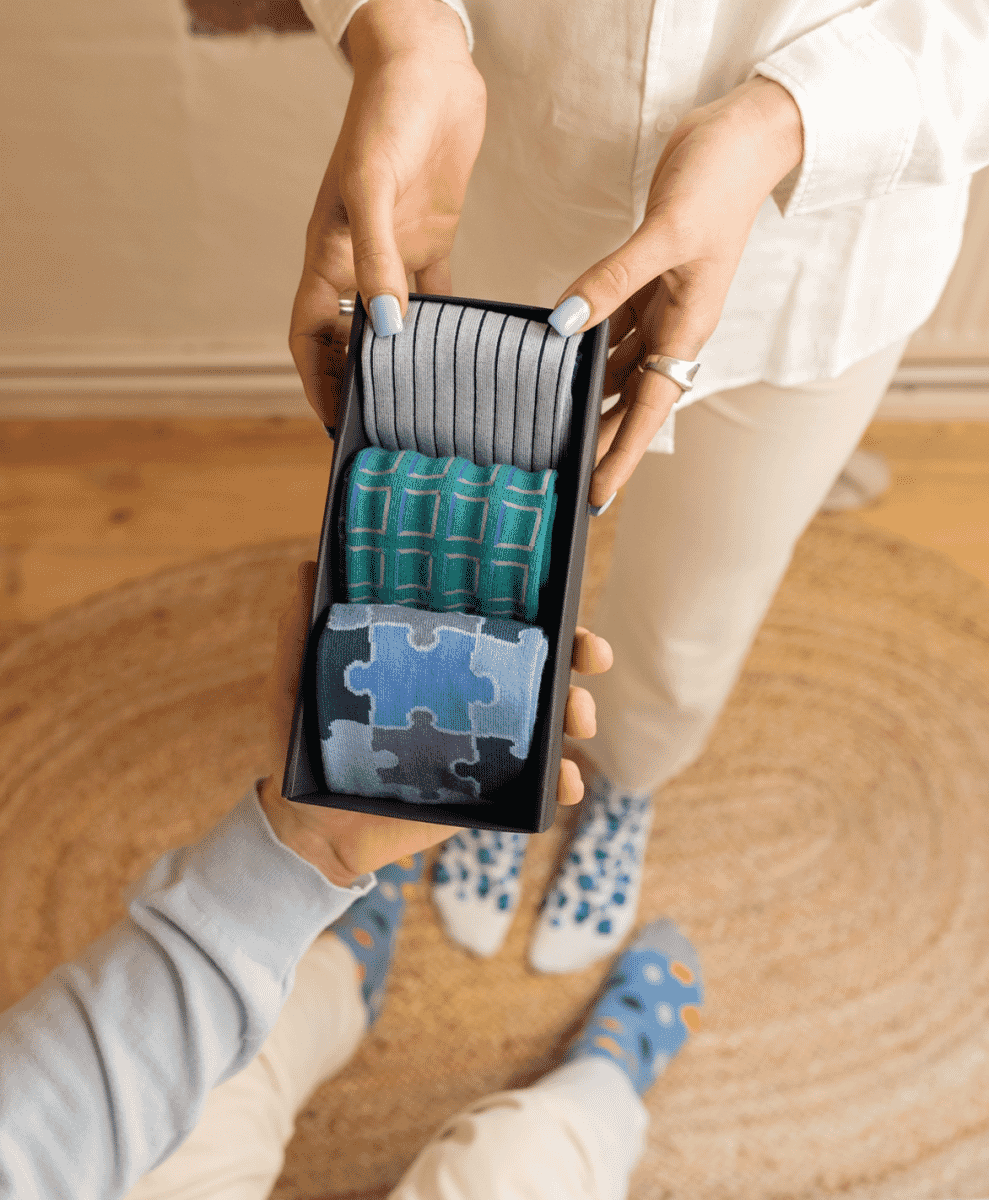 A person presenting a gift box of assorted patterned socks to a friend.