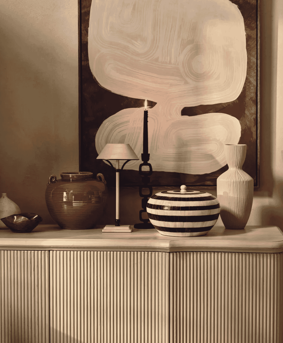 Console table vignette with ceramic vases, a lamp, and abstract art in sepia tones.