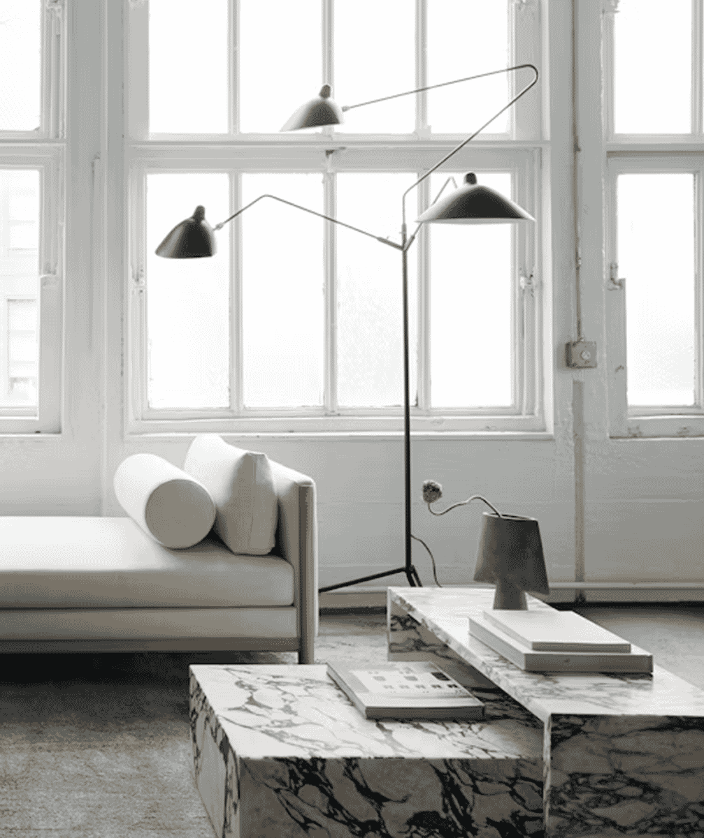 A white minimalist living room featuring the black Serge Mouille three-arm floor lamp as a focal point.