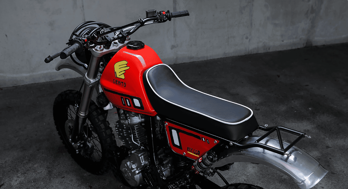 Low-angle stylized shot of the custom motorcycle featuring the red fuel tank against an industrial backdrop.