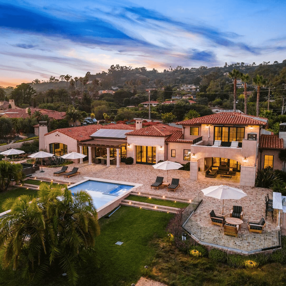 An aerial view of a luxurious Mediterranean-style estate at dusk with stone patios and a pool.