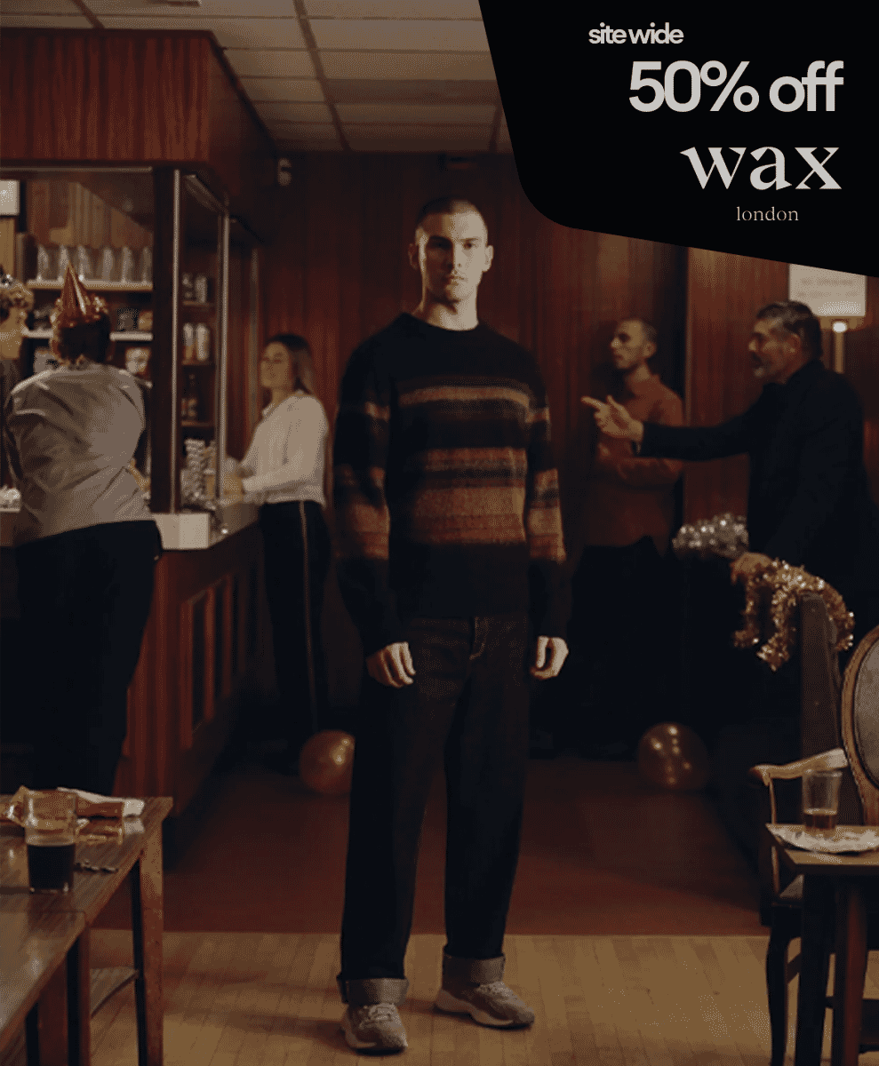 A man in a striped Wax London sweater standing in a dimly lit bar setting.