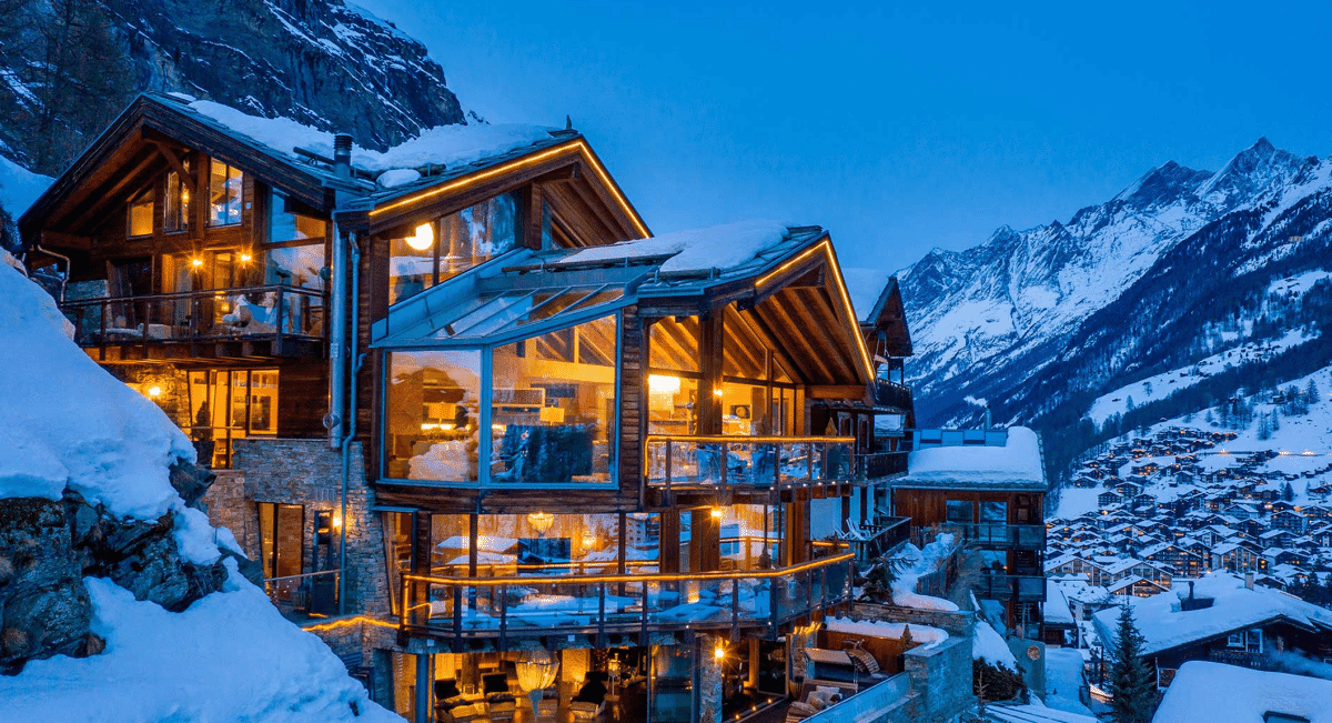 Exterior view of a luxury lodge with floor-to-ceiling glass windows illuminated from within.