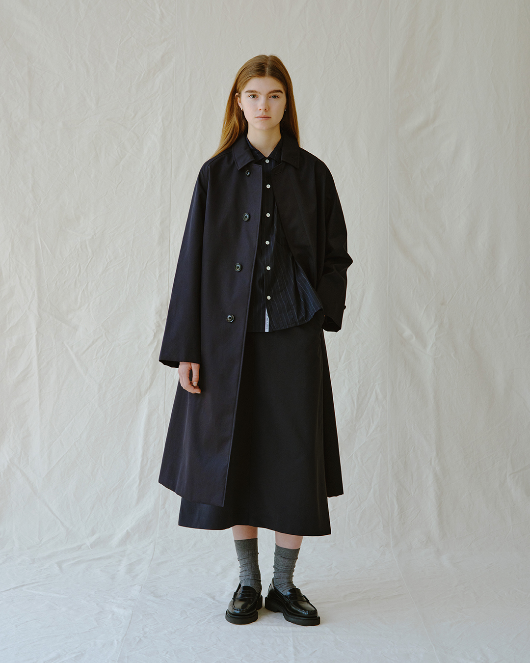 Oversized navy coat layered over a striped shirt and midi skirt.