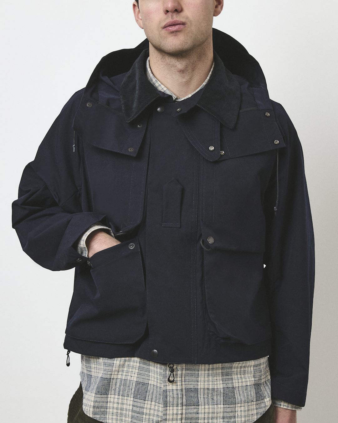 Man modeling a navy waxed cotton jacket with a corduroy collar and flap pockets over a plaid shirt.