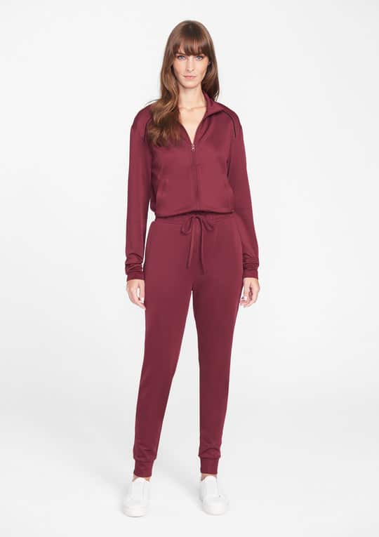 Woman wearing a maroon zip-up jogger set and white sneakers.