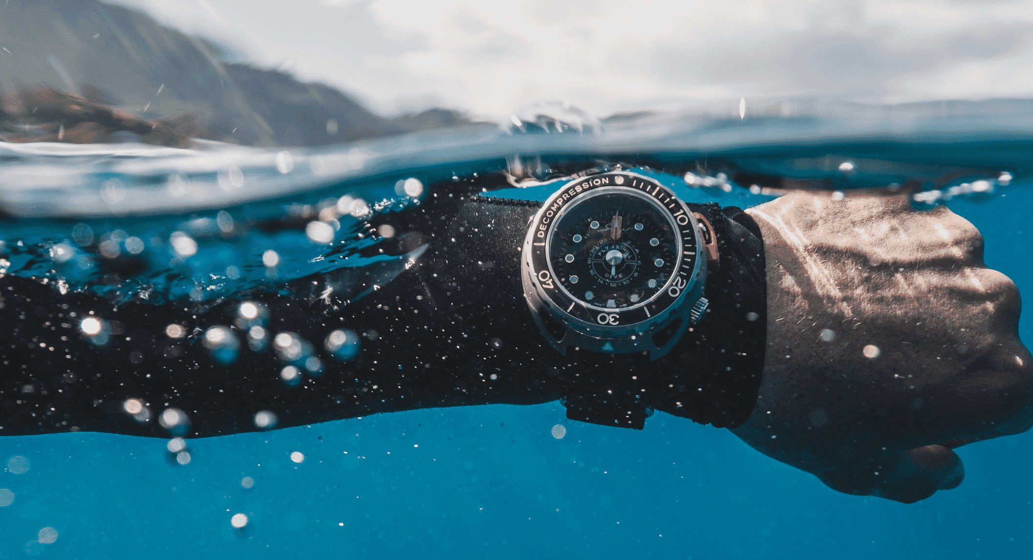 A rugged black dive watch with a decompression scale worn by a diver in clear blue water.