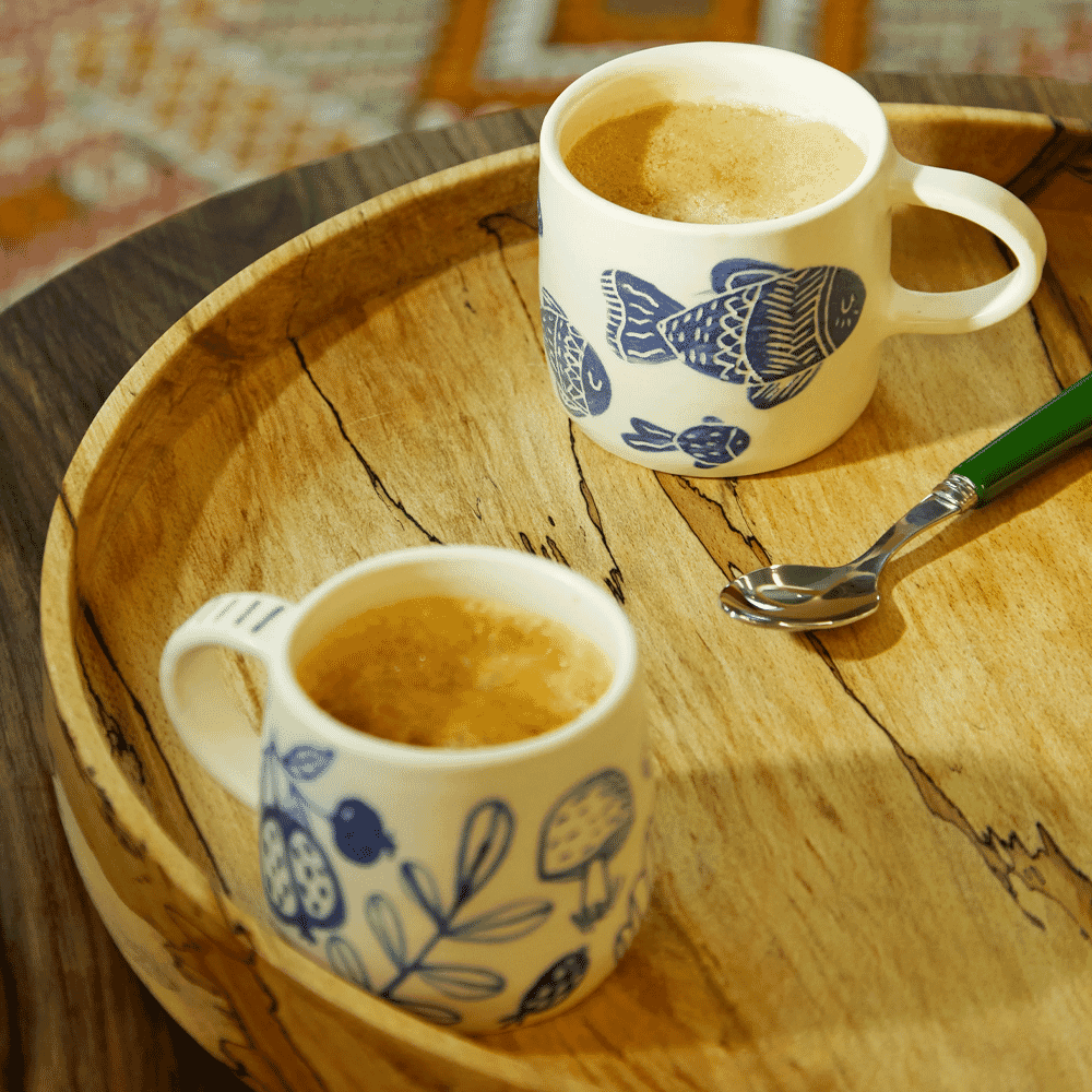 Two ceramic mugs with blue fish patterns on a wooden tray with coffee.