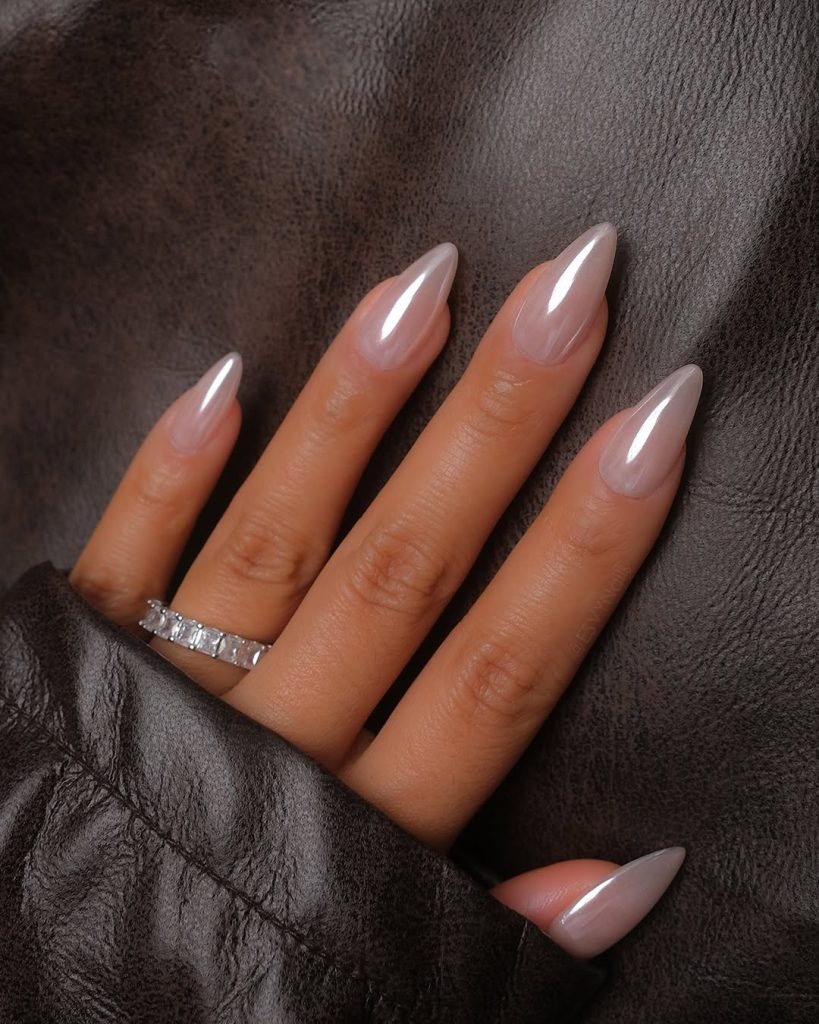 Long almond-shaped nude nails resting on a dark brown leather jacket.