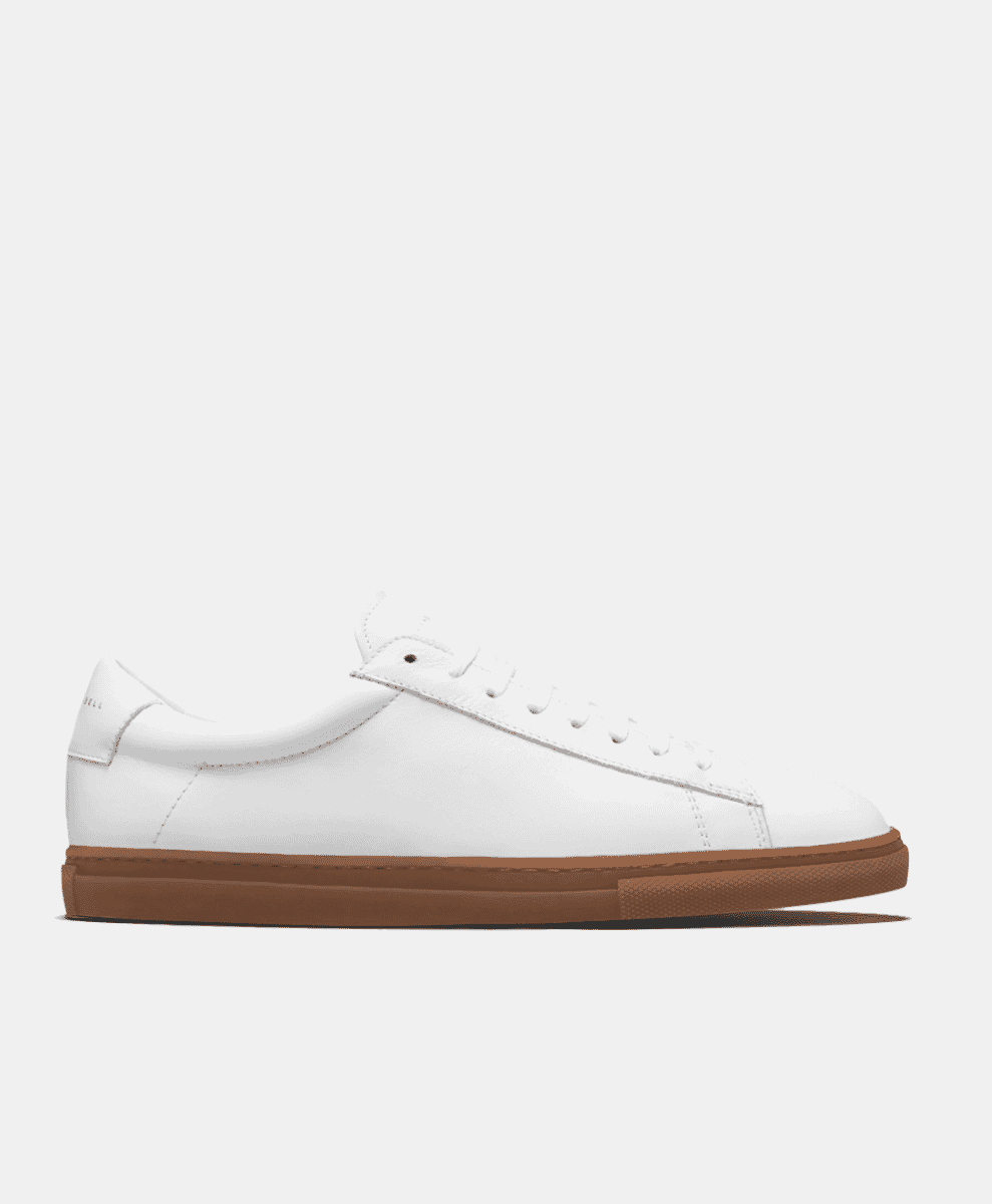 Side profile of a minimalist white leather sneaker with a brown rubber sole.