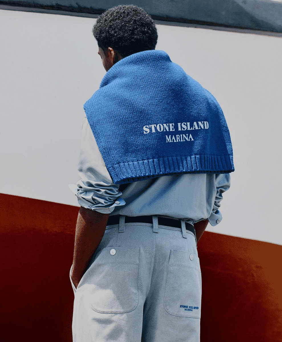 A man with a blue sweater draped over his shoulders standing against a white and red maritime backdrop.