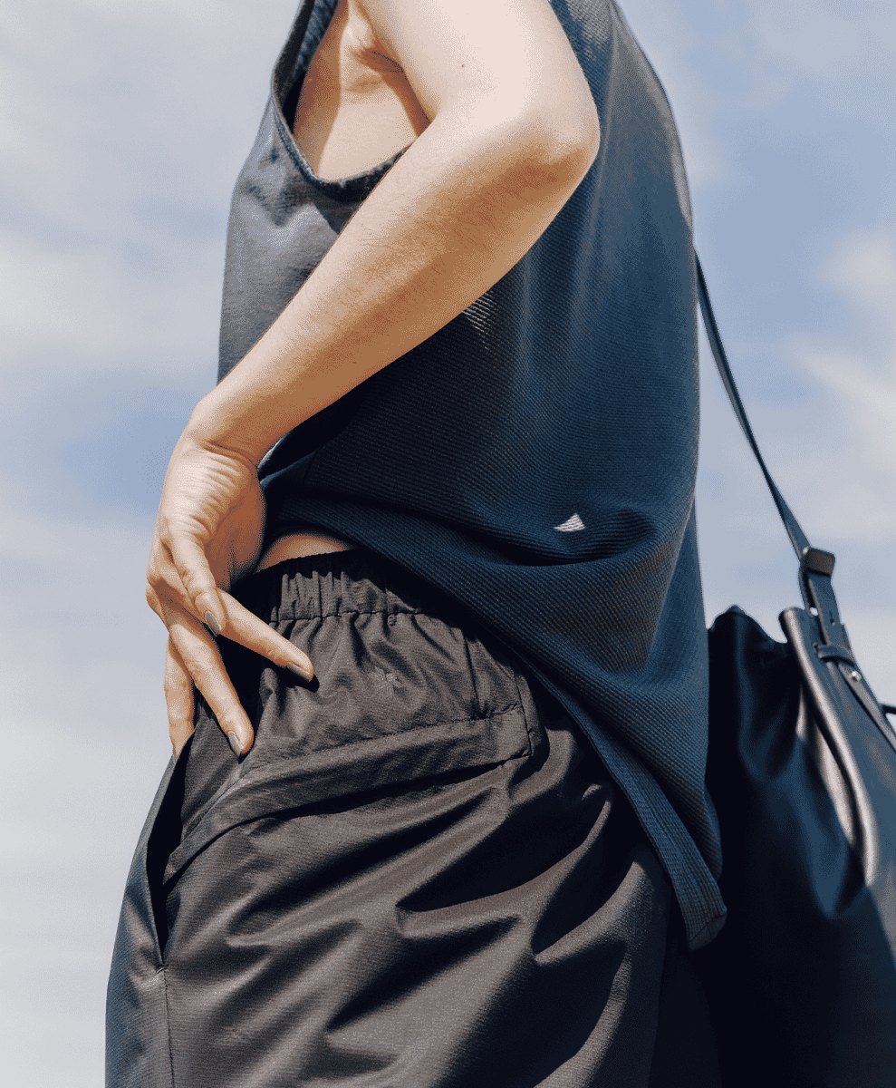 Close-up of a person in a dark ribbed tank top and black elastic-waist pants against an overcast sky.