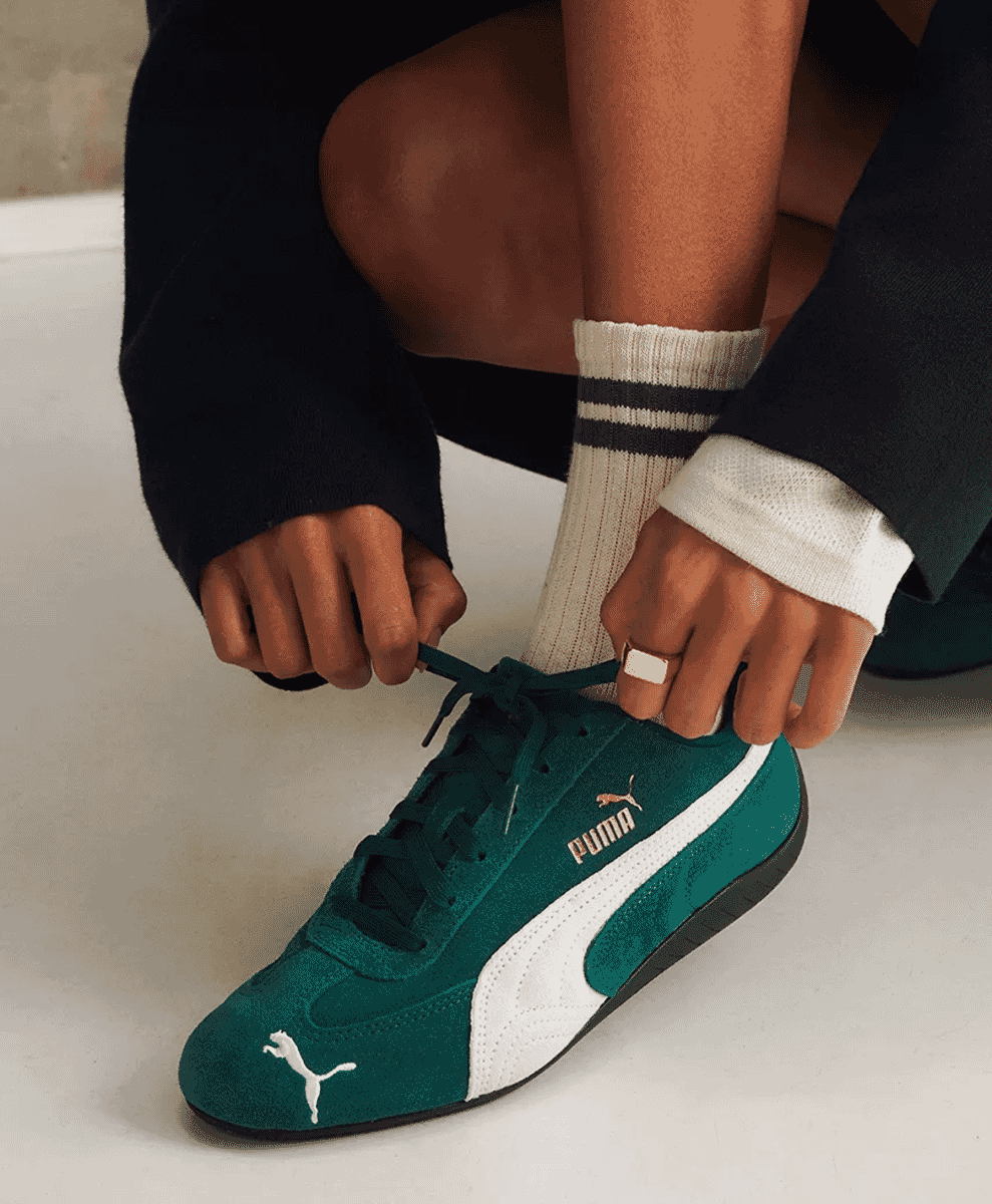 Close-up of a person tying the laces of a green suede Puma Speedcat sneaker.